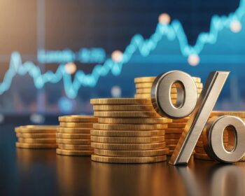 Stacks of gold coins with a large metallic percent sign in the foreground and a blurred blue stock chart in the background, signaling financial growth.