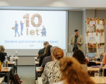 Speaker presenting a Tesco event in a conference room, large screen shows